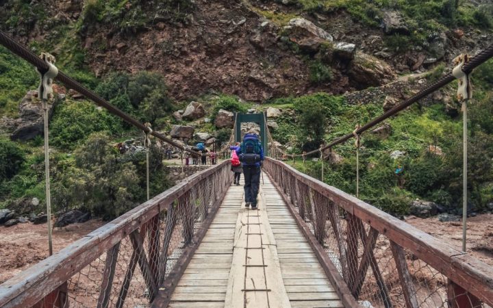 Male backpacker crossing the bridge over Vilcanota river to start inca trail to Machu Picchu archaeological site from the Inca's ancient civilization in Peru. South America
